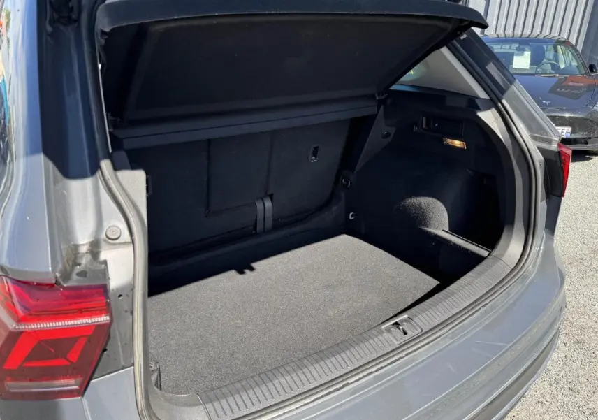 Coffre ouvert côté arrière droit d’un Volkswagen Tiguan 2.0 TDI gris, montrant un espace de chargement propre et spacieux.