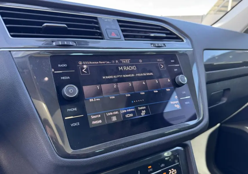 Écran tactile central du tableau de bord du Volkswagen Tiguan 2.0 TDI gris, affichant la radio FM en intérieur lumineux.