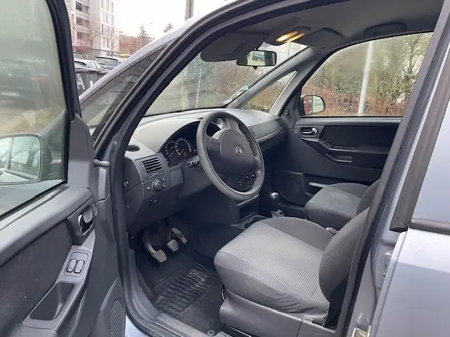 Intérieur avant gauche de l’Opel Meriva grise 2010, montrant le tableau de bord et les sièges tissu gris.