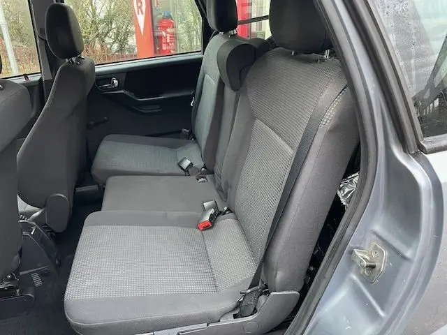 Vue intérieure côté droit sur les sièges arrière gris de l'Opel Meriva A Ph2 2010, banquette 3 places avec ceintures visibles.