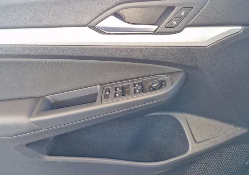 Gros plan sur la porte côté conducteur de la Volkswagen Golf A8 gris Urano, montrant les commandes des vitres et des rétroviseurs.