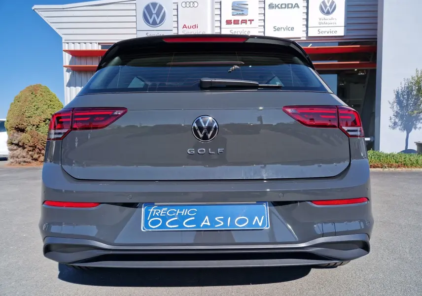Vue arrière d'une Volkswagen Golf A8 gris Urano, avec feux rouges allongés et plaque d'occasion bleue visible.