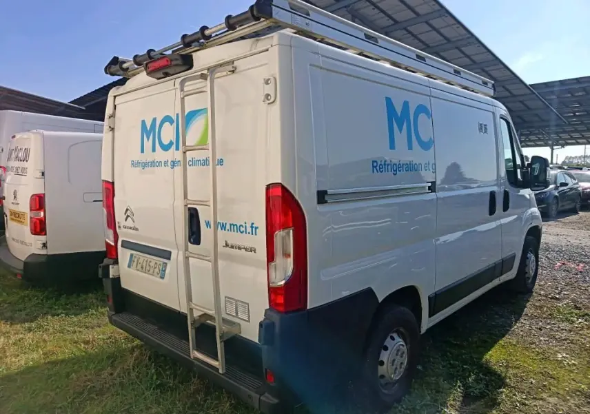 Vue 3/4 arrière droite d'un utilitaire Citroën Jumper blanc avec galerie et marquage publicitaire MCI sur les côtés et portes arrière.