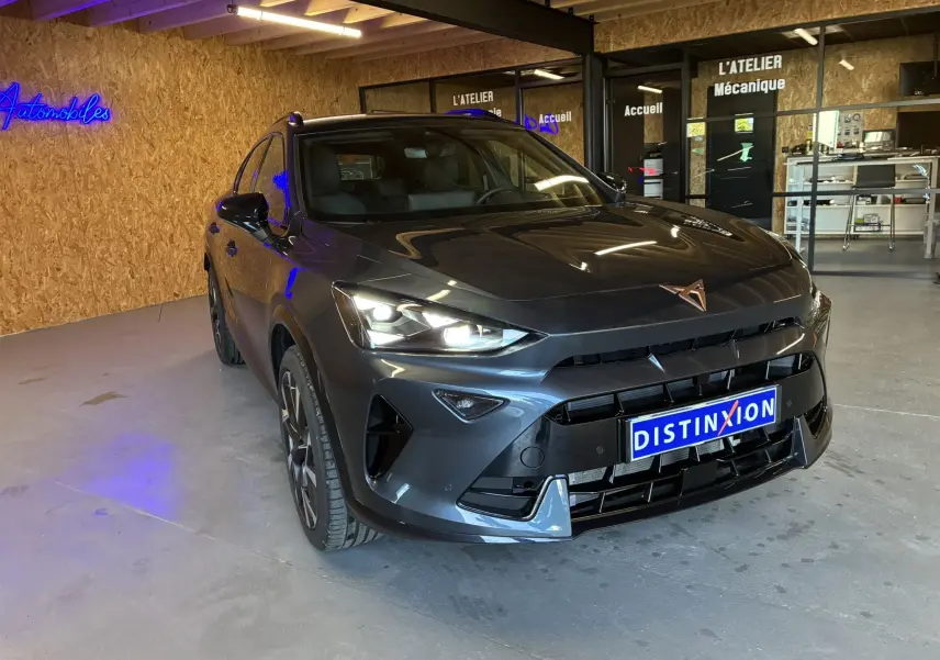 Vue 3/4 avant d'une CUPRA Formentor gris foncé avec phares allumés dans un garage moderne.