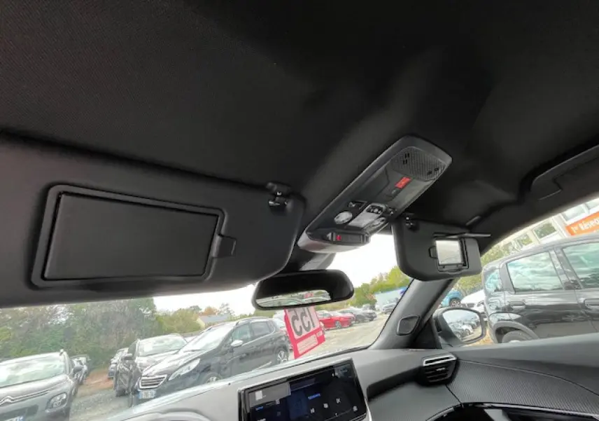 Vue intérieure avant du Peugeot 2008 blanc Okenite, montrant le tableau de bord et les pare-soleil avec miroirs intégrés.