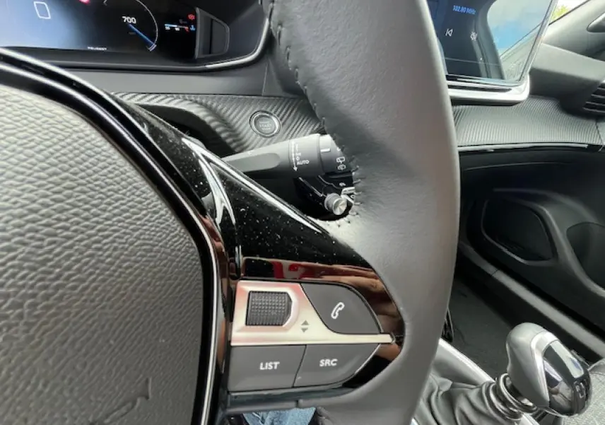 Vue rapprochée du volant et levier de vitesse manuel du Peugeot 2008 blanc, avec commandes audio intégrées et tableau de bord numérique.