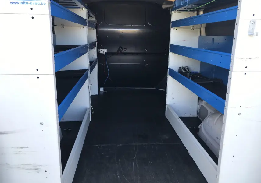 Intérieur du coffre d’un Volkswagen Transporter T6 blanc, vue de l’arrière montrant des étagères blanches et bleues de chaque côté.