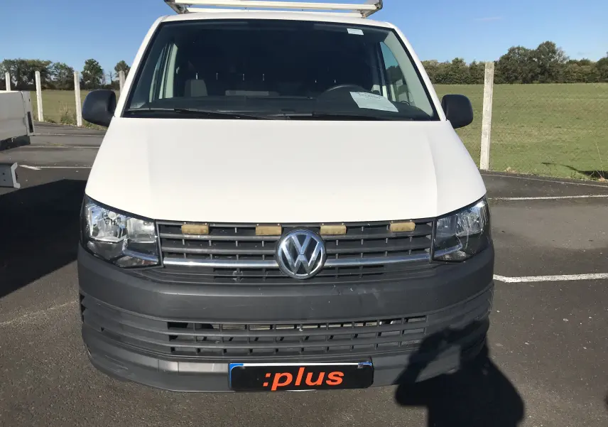 Vue frontale d'un Volkswagen Transporter T6 blanc avec calandre noire et plaque d'immatriculation :plus visible.