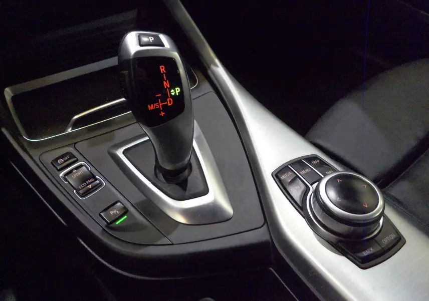 Gros plan sur la console centrale de la BMW Série 1 F21 LCI 118i gris, mettant en valeur le levier de vitesses automatique et les commandes multimédia.