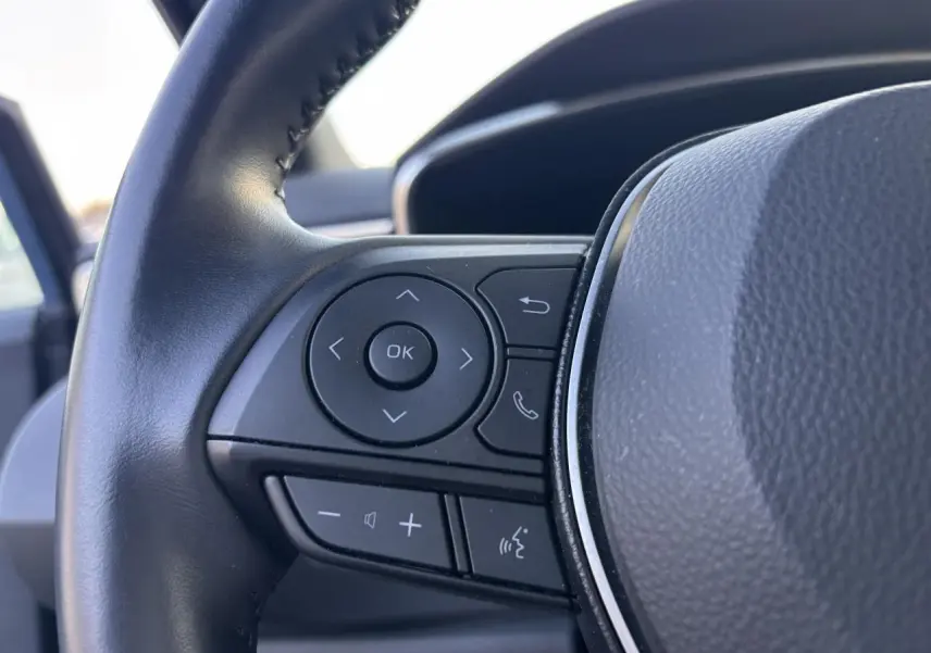 Gros plan sur les commandes multifonctions à gauche du volant en cuir noir de la Toyota Corolla hybride bleu clair 2020.