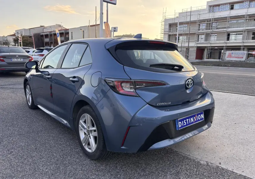 Vue 3/4 arrière droite d'une Toyota Corolla hybride bleu clair 2020 avec finition Dynamic Business sur parking extérieur.
