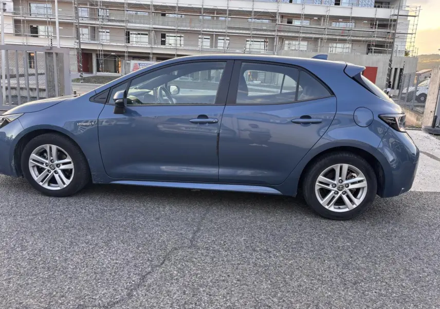 Profil côté gauche d'une Toyota Corolla hybride 2020 bleu clair, berline compacte avec jantes alliage et badge Hybrid visible.