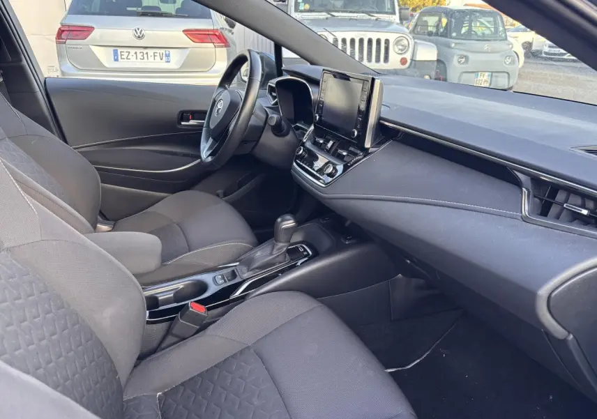Intérieur avant droit de la Toyota Corolla hybride 2020, montrant sièges noirs, volant, console centrale et écran tactile.