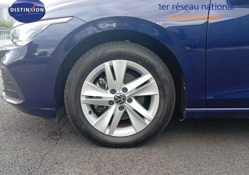 Gros plan sur la roue avant gauche d'une Volkswagen Golf VIII bleu Atlantique métal avec jante alliage 16 pouces.