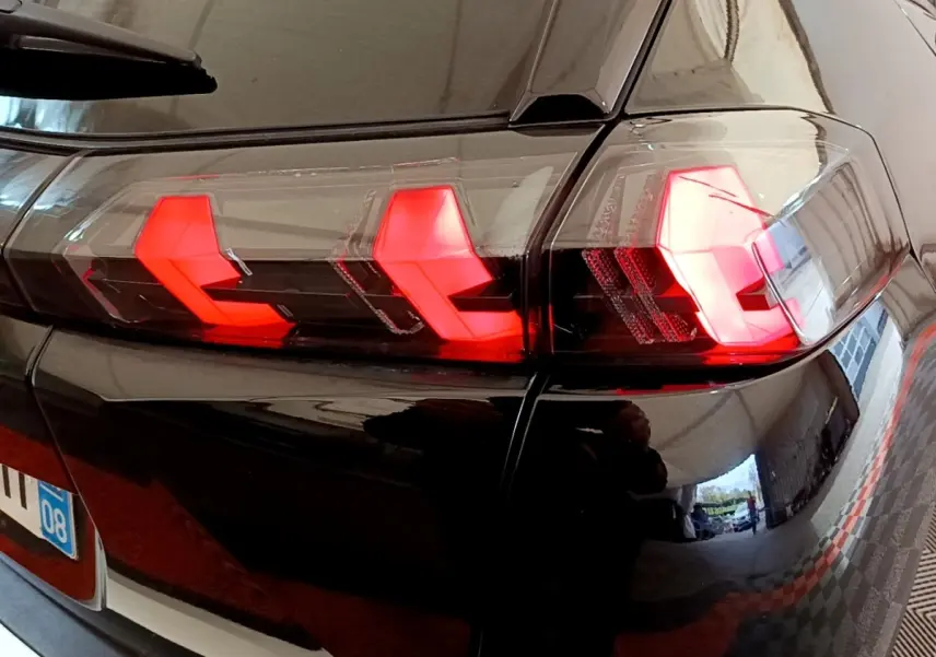Gros plan sur le feu arrière droit rouge d’un Peugeot 2008 noir, reflétant l’environnement intérieur.