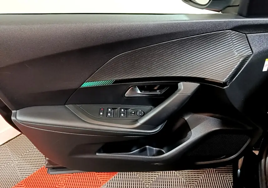 Vue intérieure côté gauche de la porte avant d’un Peugeot 2008 noir avec insert effet carbone et commandes électriques.