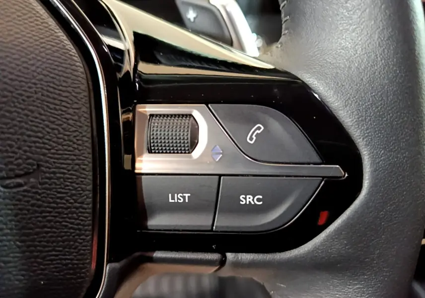 Gros plan sur les commandes multifonctions noires du volant cuir du Peugeot 2008 noir, version BlueHDi 130.