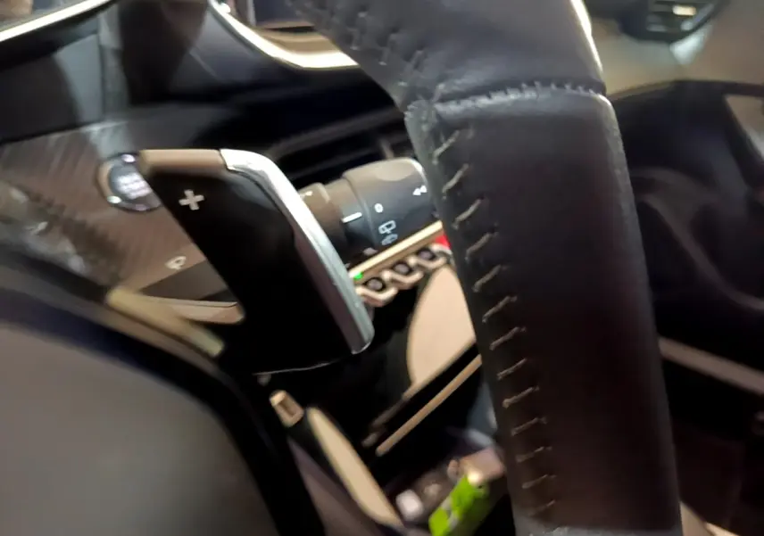 Gros plan sur le volant cuir noir et la palette de changement de vitesse + du Peugeot 2008 Diesel 2021, intérieur moderne.