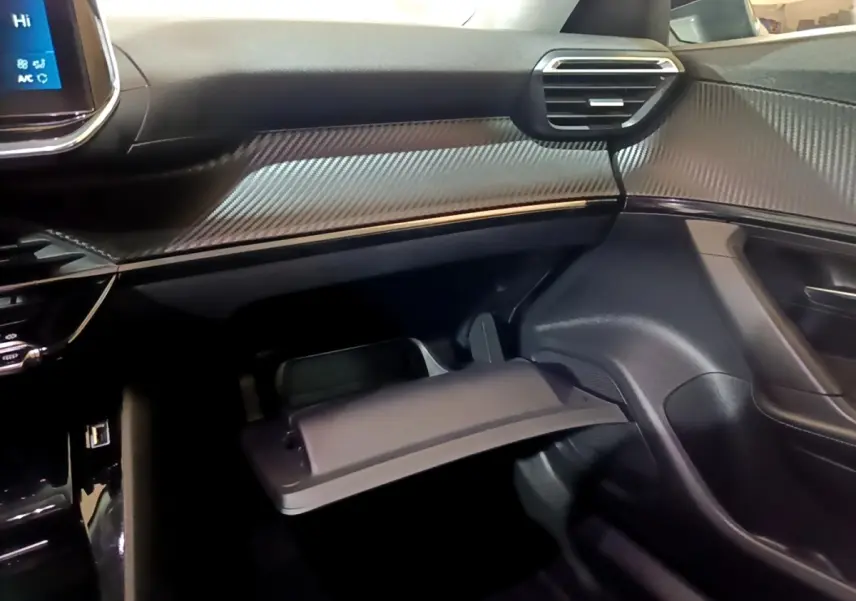 Intérieur côté passager du Peugeot 2008 2021 noir, montrant la boîte à gants ouverte et le tableau de bord avec finition carbone.