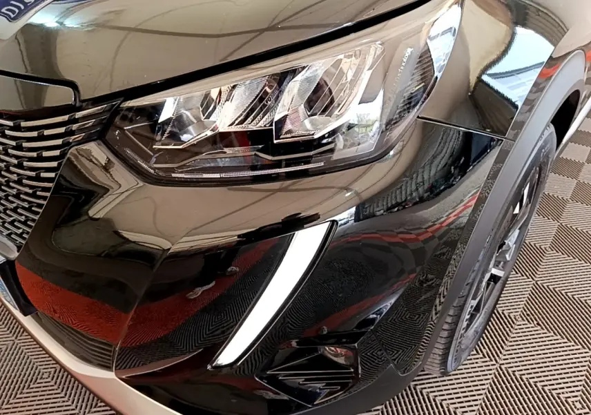 Gros plan sur l'avant droit noir brillant du Peugeot 2008 2021, mettant en valeur le phare LED et la calandre distinctive.