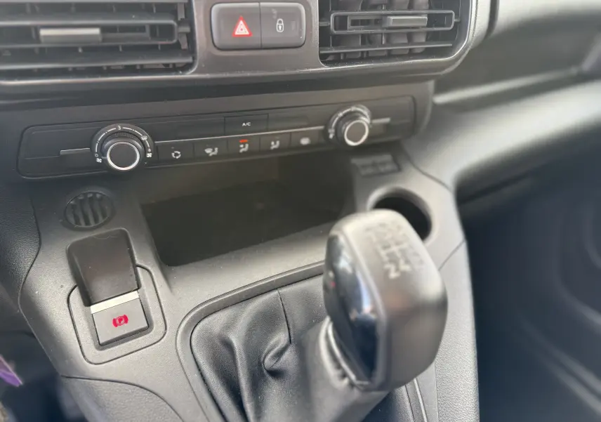 Gros plan sur la console centrale du Peugeot Partner blanc 2021, avec levier de vitesse manuel et commandes de climatisation.