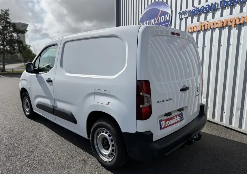 Vue 3/4 arrière droite d'un utilitaire Peugeot Partner blanc 2021 avec attelage et porte latérale pleine.