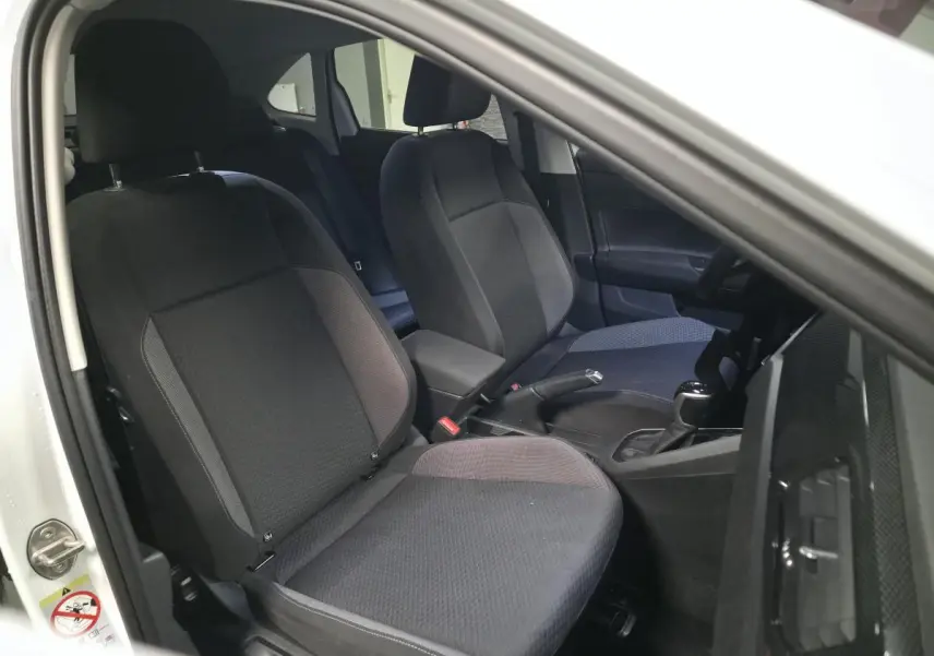 Vue intérieure côté conducteur du Volkswagen Taigo blanc 2024, sièges en tissu gris et console centrale avec levier de vitesse.