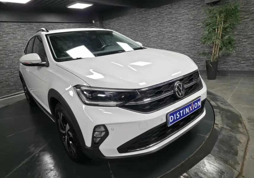 Vue 3/4 avant droite du Volkswagen Taigo blanc avec calandre noire et projecteurs LED dans un showroom.