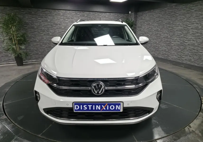 Vue frontale d'un Volkswagen Taigo blanc avec calandre noire et logo VW centré, en showroom intérieur.