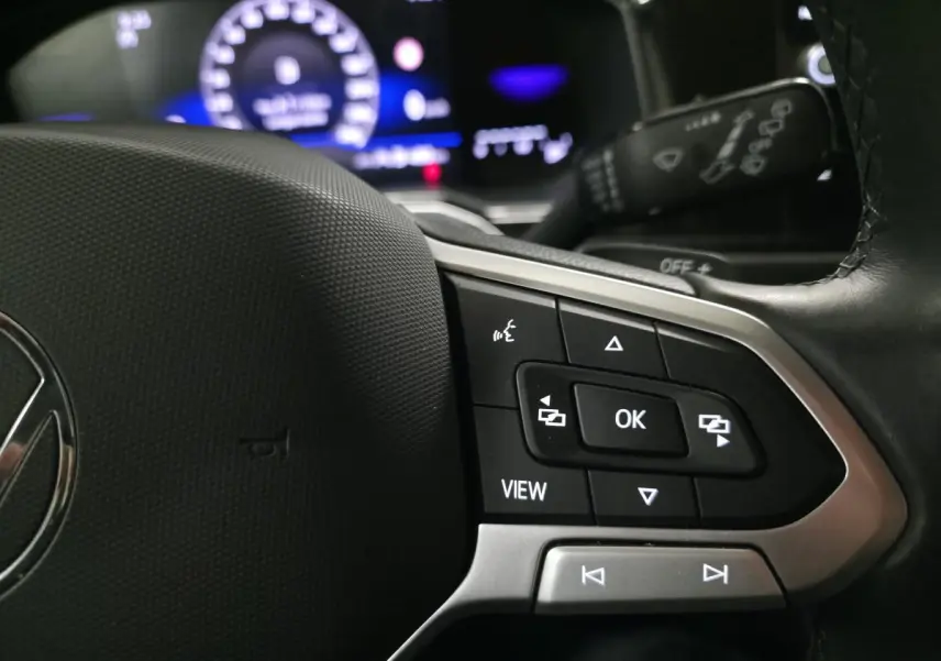 Gros plan sur les commandes multifonctions du volant cuir du Volkswagen Taigo 2024 avec affichage digital en arrière-plan.