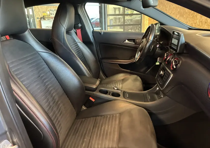 Vue intérieure côté conducteur de la Mercedes Classe A 250 AMG Sport 2014 avec sièges cuir noir et détails rouges.
