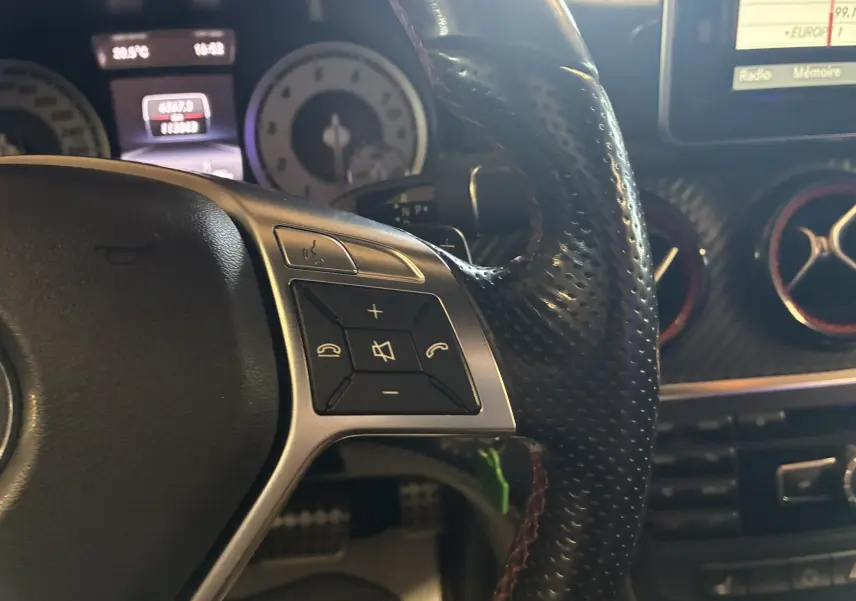 Gros plan sur le volant perforé noir de la Mercedes Classe A 250 AMG Sport gris, avec commandes audio intégrées.