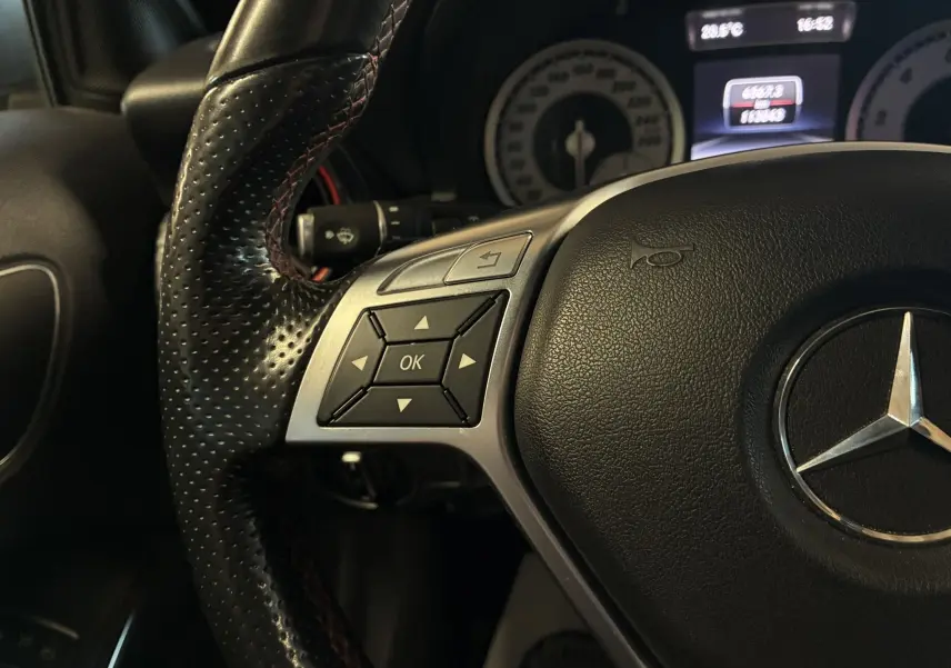 Gros plan sur le volant cuir perforé côté gauche d'une Mercedes Classe A 250 AMG Sport gris, avec commandes intégrées.