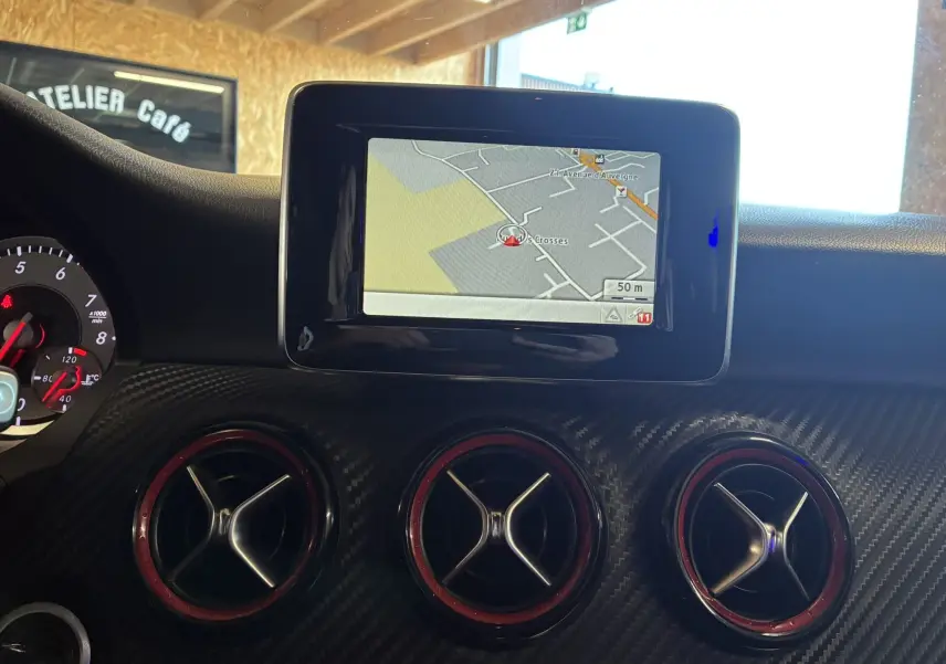 Vue intérieure du tableau de bord d'une Mercedes Classe A 250 AMG Sport 2014, avec écran GPS et aérateurs ronds à bordure rouge.
