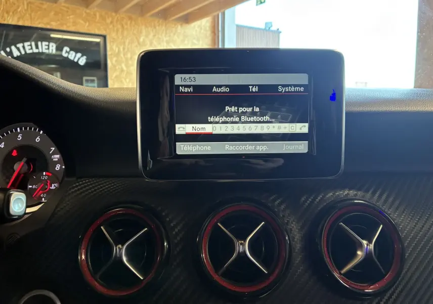 Vue rapprochée de l'écran central et des aérateurs rouges du tableau de bord carbone d'une Mercedes Classe A 250 AMG Sport gris.