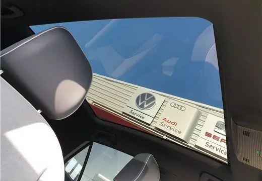 Vue intérieure du toit ouvrant du Volkswagen ID.3 blanc glacier, avec vue sur enseignes VW et Audi Service à l'extérieur.