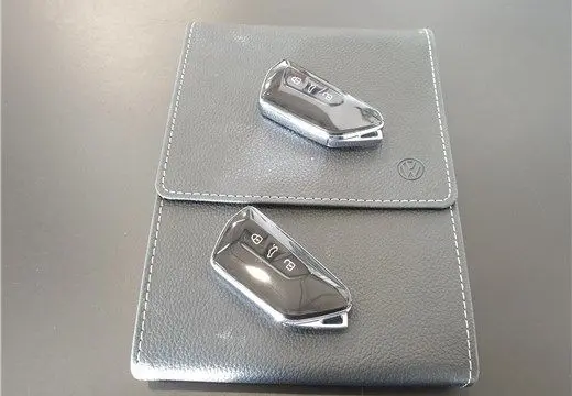 Deux clés de voiture Volkswagen posées sur une pochette en cuir gris avec logo VW, vue de dessus, sans véhicule visible.