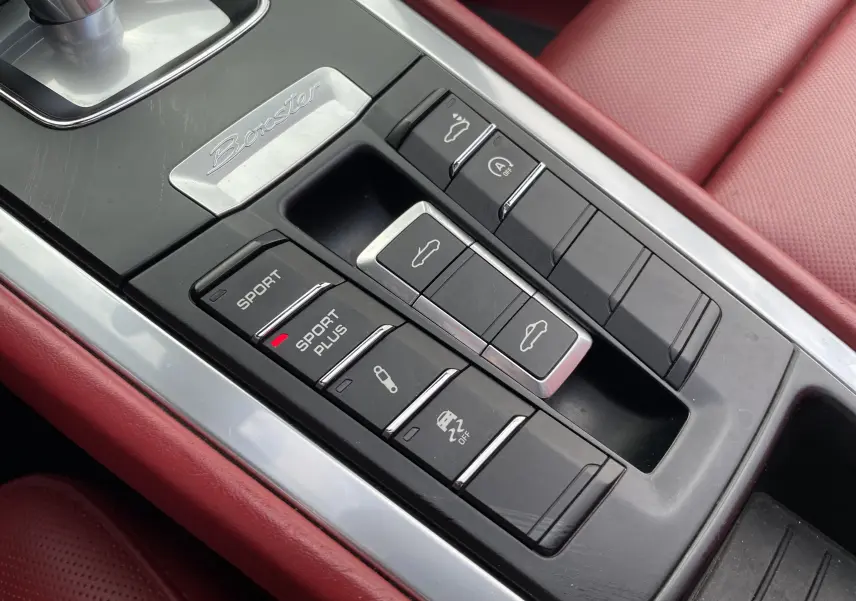Gros plan sur la console centrale noire et cuir rouge grenat de la Porsche Boxster S 981 avec boutons Sport Plus et ouverture capotes.