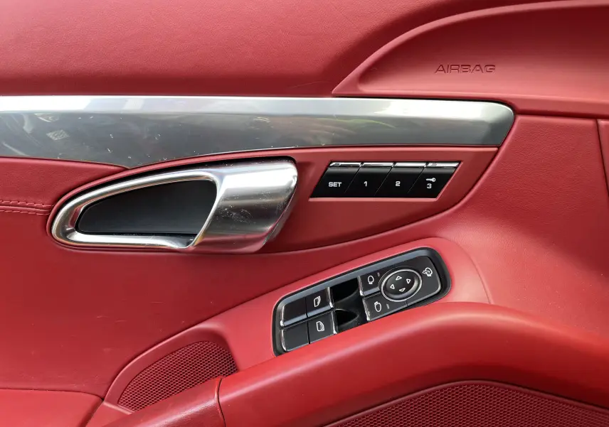 Détail de la porte côté gauche en cuir rouge grenat avec poignée alu et commandes mémoire sur Porsche Boxster S 2012.
