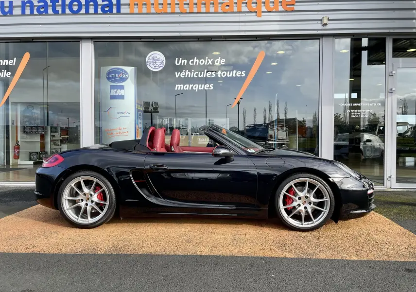 Profil droit d'une Porsche Boxster S 981 noire intense avec intérieur cuir rouge grenat et jantes Carrera 20 pouces.