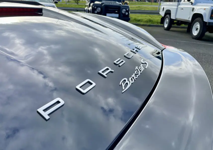 Gros plan sur l'arrière noir intense brillant d'une Porsche Boxster S, mettant en valeur le logo et l'inscription du modèle.