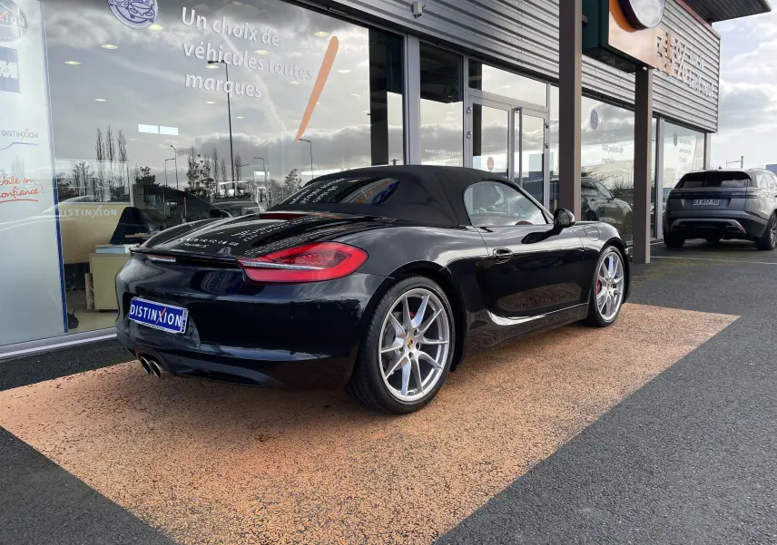 Vue 3/4 arrière droite d'une Porsche Boxster S noire intense avec capote noire et jantes Carrera S 20 pouces.