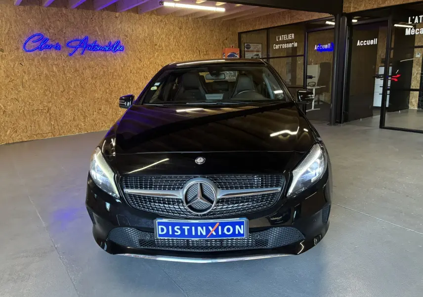 Vue avant d'une Mercedes Classe A 180 CDI Sensation noire, avec calandre étoilée et plaque Distinxion en intérieur showroom.