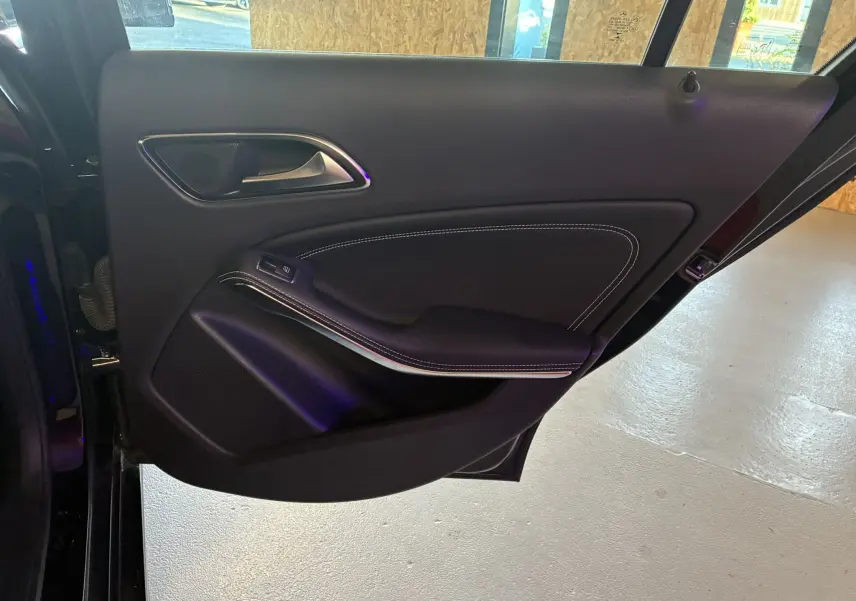 Gros plan sur la porte arrière gauche noire d'une Mercedes Classe A 180 CDI 2018, avec garniture cuir et surpiqûres blanches.