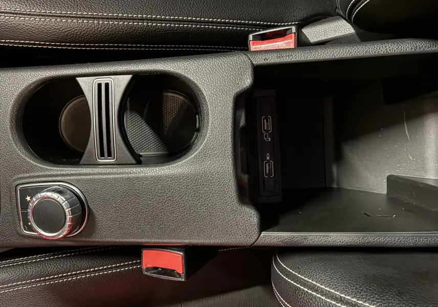 Gros plan sur la console centrale noire de la Mercedes Classe A 180 CDI 2018, avec porte-gobelets et ports USB visibles.