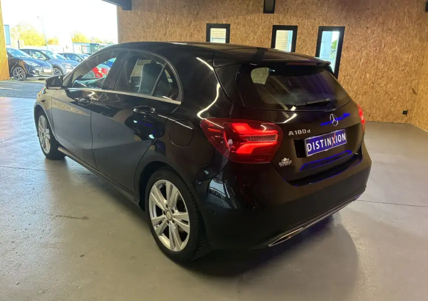 Mercedes Classe A 180 CDI noir vue 3/4 arrière droit en intérieur, feux arrière allumés et jantes argentées visibles.
