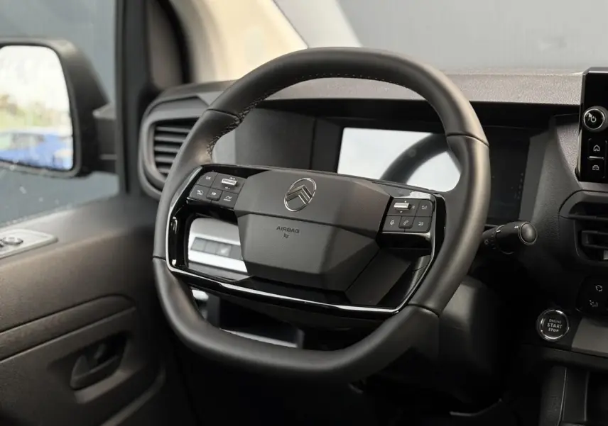 Vue intérieure centrée sur le volant cuir noir du Citroën Jumpy 2025 avec commandes intégrées et tableau de bord numérique.