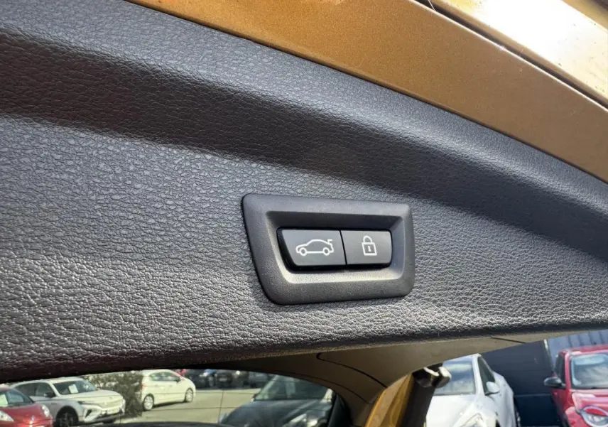 Gros plan sur les boutons d'ouverture et de verrouillage du hayon du BMW X2 jaune, vue intérieure arrière du coffre.
