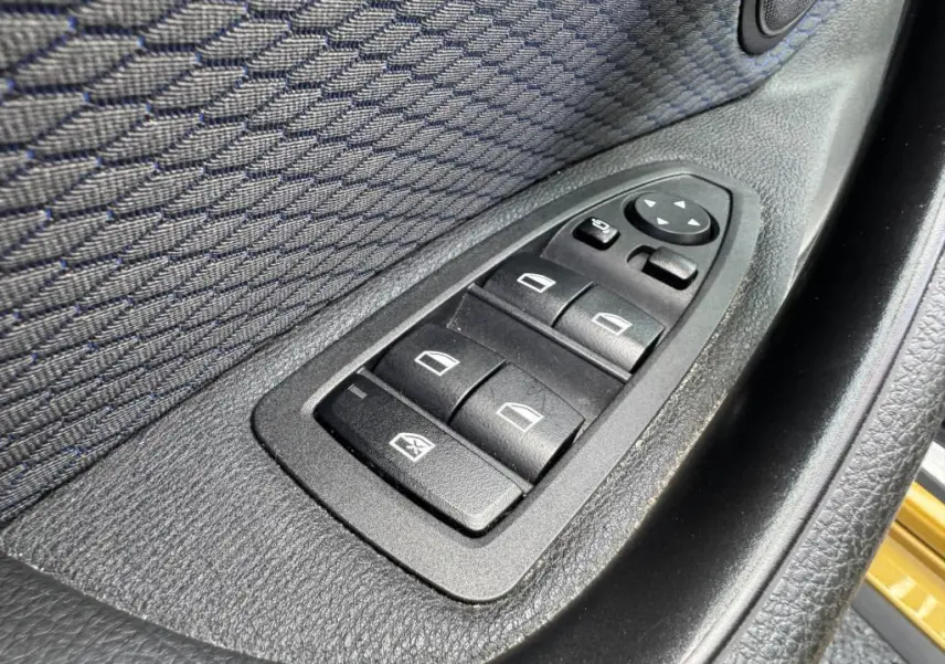 Gros plan sur les commandes des vitres électriques côté conducteur d'une BMW X2 jaune 2021, finition M Sport.