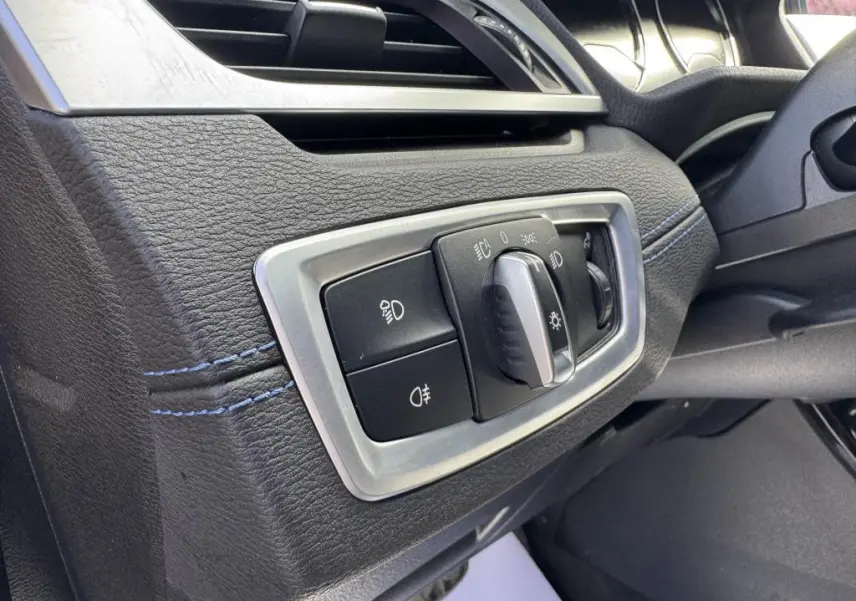 Gros plan sur le bouton de commande des phares à gauche du volant dans l’habitacle noir avec surpiqûres bleues du BMW X2 jaune M Sport 2021.